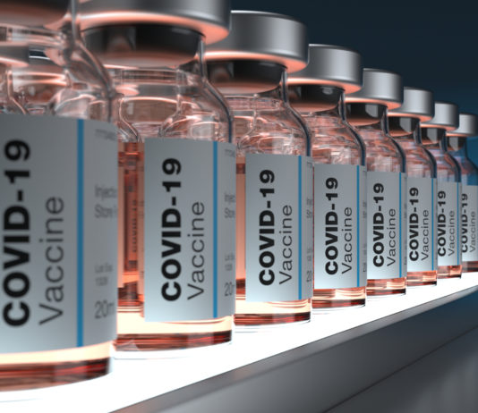 Budget Week at the Georgia Legislature PODCAST COVID-19 vaccines: Clear bottles of the pale pink liquid vaccine labeled and ined up on a shelf in a semi-dark room