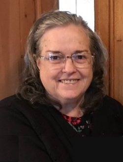 Smiling woman with shoulder-length brown and grey hair, wire-rim glases and a black top.