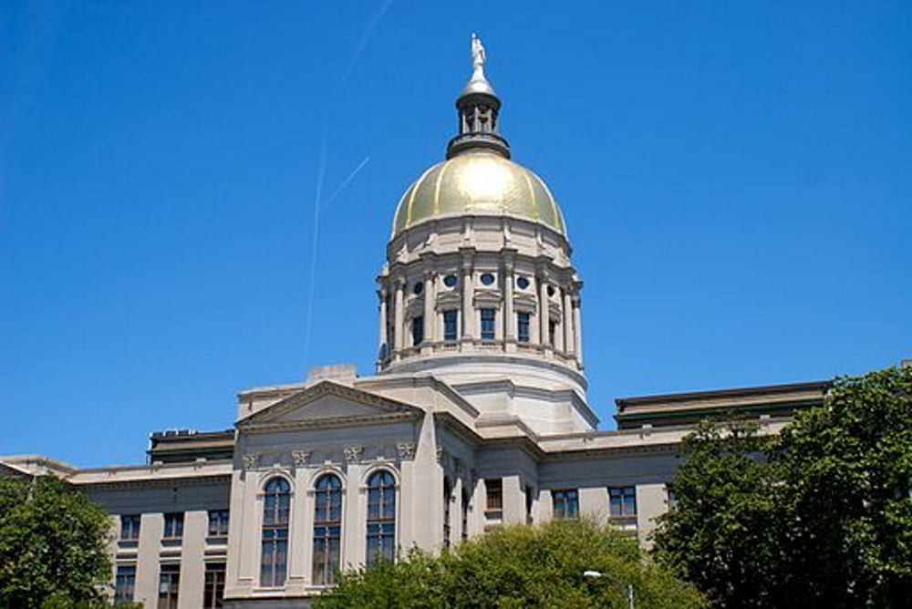 Georgia's gold dome Capitol building in Atlanta. surrounded by grren trees against a cloudless, bright blue sky.