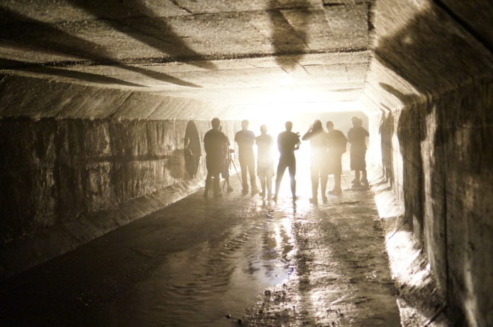 Gang violence: Group of people in hoodies and pants stand facing a bright light at the far end of a fog-filled tunnel
