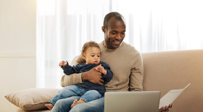 A controversial new election law, details on the parental leave bill and a feud in the General Assembly Black man wearing beige sweater sitting on beige couch in front of white curtains holding baby in jeans and navy sweatshirt with laptop on couch