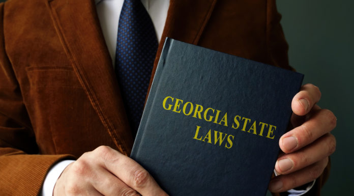 What passed and failed in 2021 Georgia General Assembly Closeup of black Georgia state law book held by man's hands wearing brown suit, white shirt and navy tie