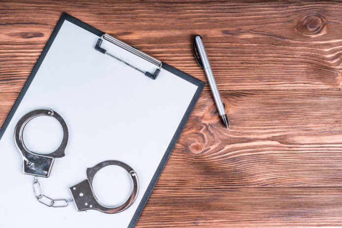 Handcuffs and clipboard with pen on wood table