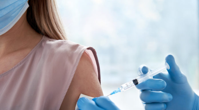 Georgia to pause use of Johnson & Johnson COVID-19 vaccine Blue-goved hands giving hypodermic shot in upper arm to blonde person wearing a beige top and blue face mask