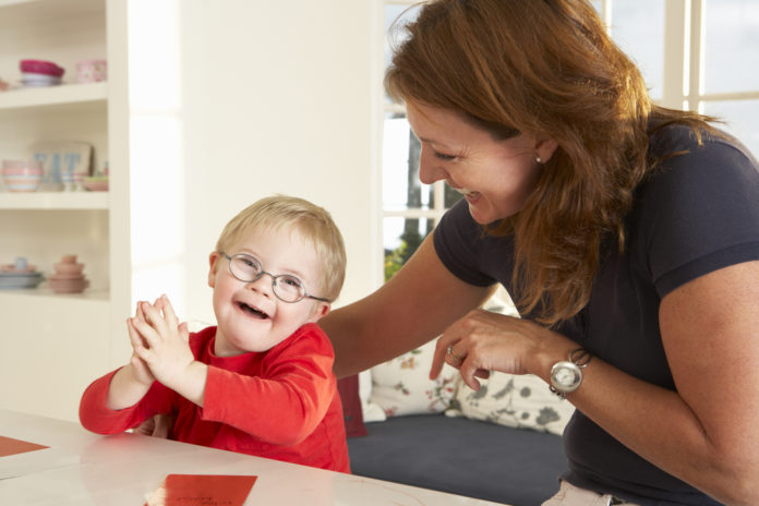 woman with brown hair wering black top and young toddler with blonde hair and glasses wearing red shirt sit at white kitchen counter