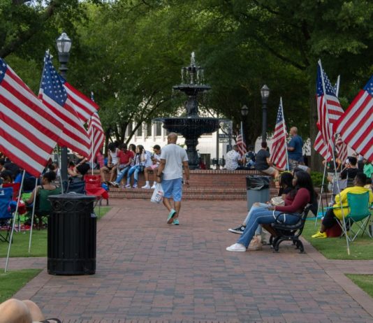 Cobb County celebrates first Juneteenth as federal holiday Crowd of people sit and stand around American flags lining brick sidewalk in park during celebration
