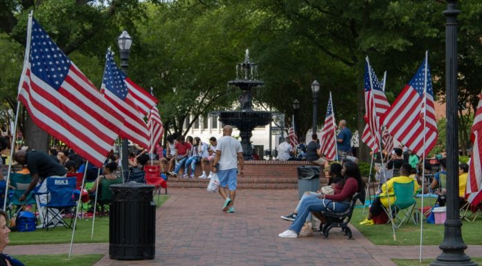 Cobb County celebrates first Juneteenth as federal holiday Crowd of people sit and stand around American flags lining brick sidewalk in park during celebration