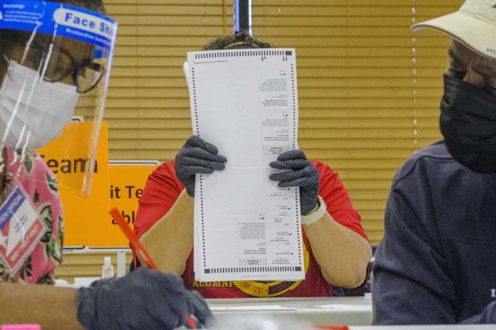 Three poll workers wearing gloves and masks counting ballot sheets