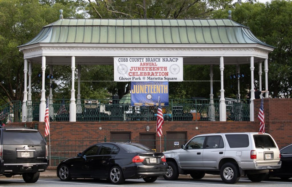 Covered gazebo with cars parked in front decorated with signs for Juneteenth