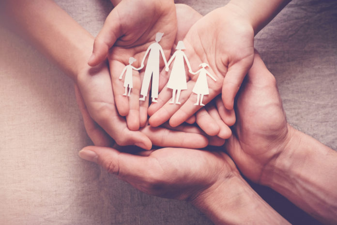 Therapeutic foster care: Hands palms up overlapping holding paper cutout of 2 adults with 2 children holding hands
