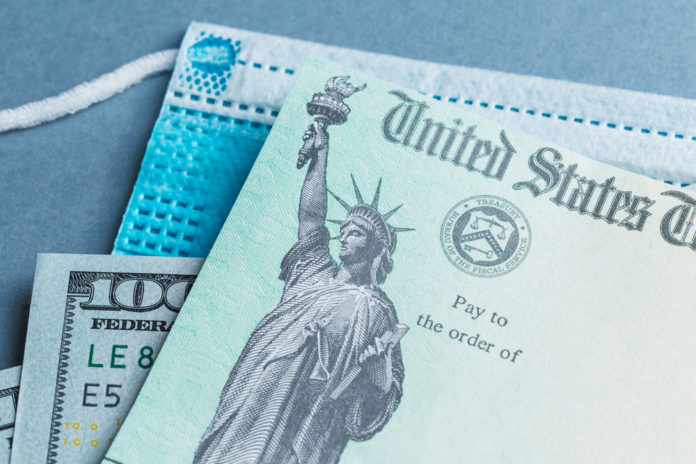 United States treasury check on top of a hundred dollar bill, on top of a blue surgical mask