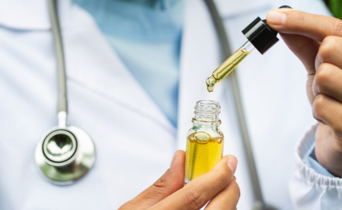 person in lab coat holding thc oil with hemp plants