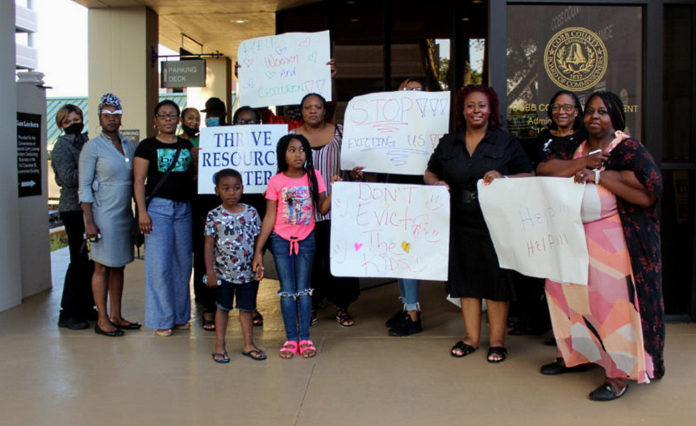 Cobb County residents protest: group of adults an two young children stand with portest signs in in lobby of modern building with Cobb County seal on doors