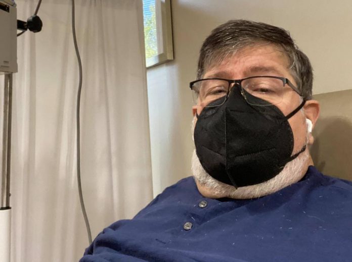 protests against Georgia regents' precautions: white man wearing mask and earbuds sits in a chair