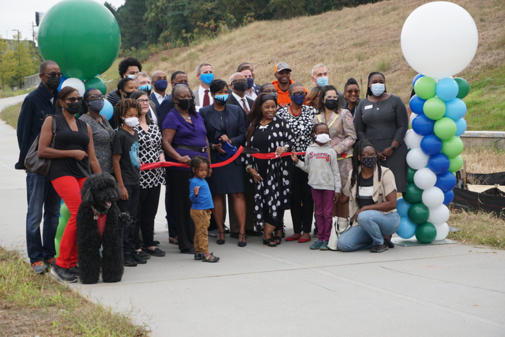 large group of people standing between two ballon statutes with two people holding a red ribbon for a ribbon cutting 
