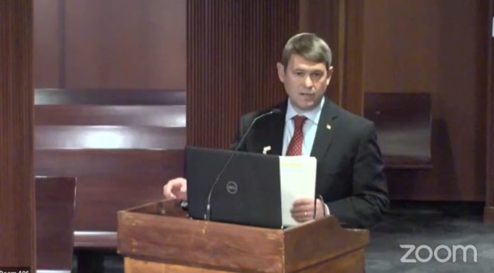 Experts warn of fiscal impact of new cities white man in grey suit with a white button down and red tie in front of a wooden podium with a dell laptop open on top