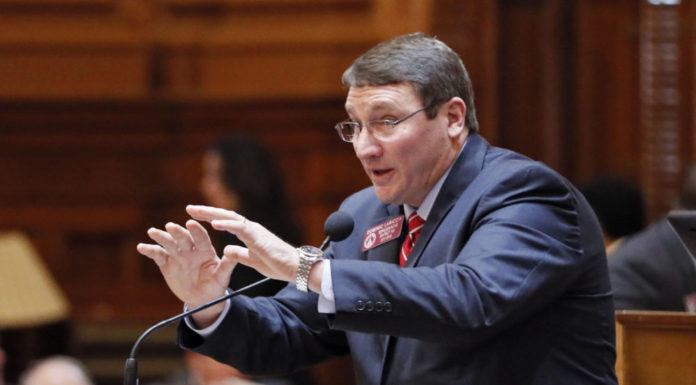 For paired Georgia House members, tough election bids loom Redistricting debate: white man with arms out stretched in a navy blue suit with whit shirt with red tie behind podium with mic