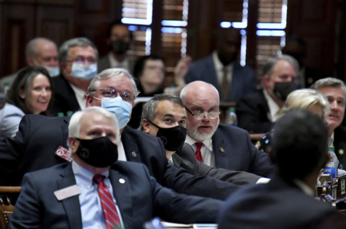 Redistricting in Georgia: men and women in business cassual clothing sit in a room gathered two white men with black face mask on , one with a blue surgical mask and glasses on