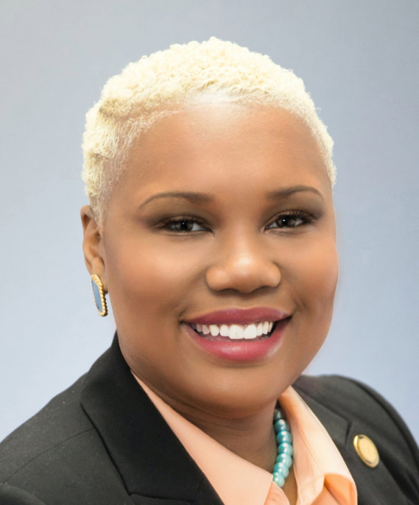 Redistricting map Final: Headshot of blonde-haired smiling Black woman with buzz cut wearing black jacket and peach blouse