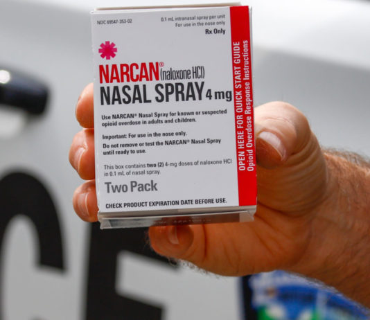 Addiction recovery community asks state to fund Narcan for EMS workers — especially rural ones a hand holding a prescription white and red drug box out of a police car