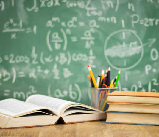 Georgia lawmakers recommend raising minimum dropout age for students books and pencils on a wooden table in front of a green chalkboard with white writing in chalk