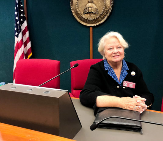 One of Georgia’s longest-serving female lawmakers reflects on her losses and wins Maray Marget Oliver: lady with short white hair blue blouse with black blazer in red chair at wooden table with American flag