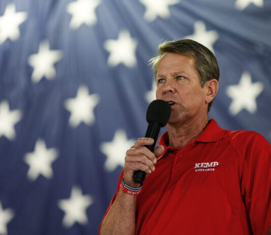 Perdue lags Kemp in fundraising in Georgia governor’s race white man holding microphone in red shirt with blue and white star background