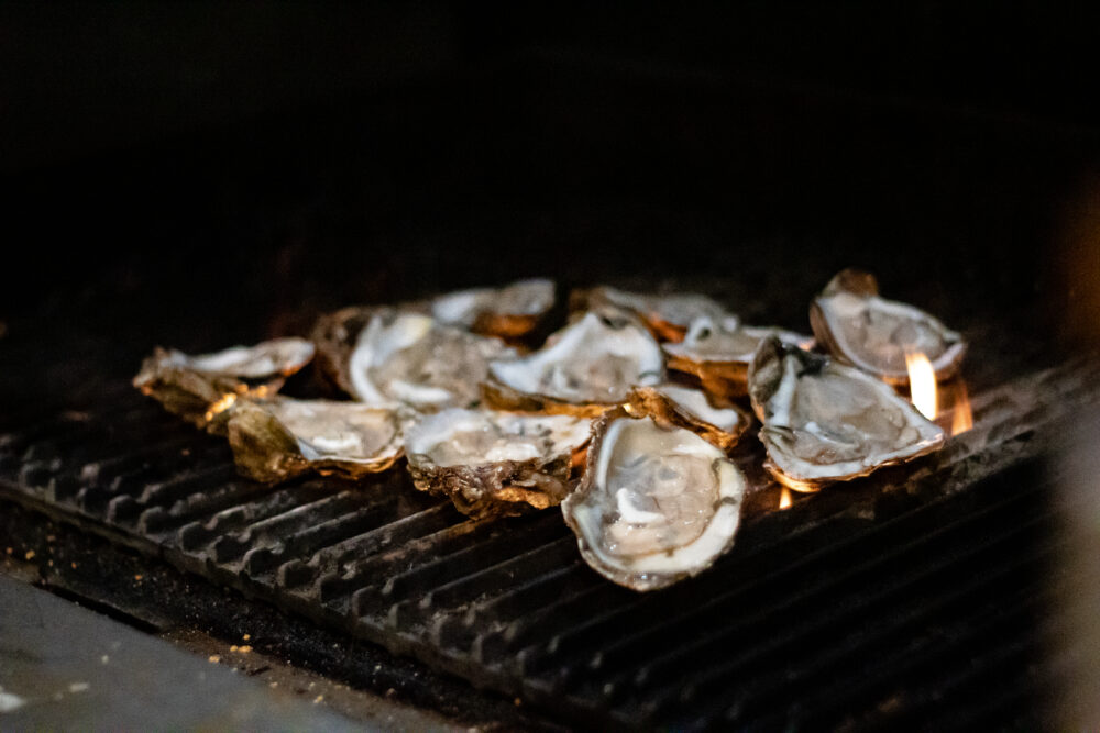 multiple half open oysters laying on top of lit grill.