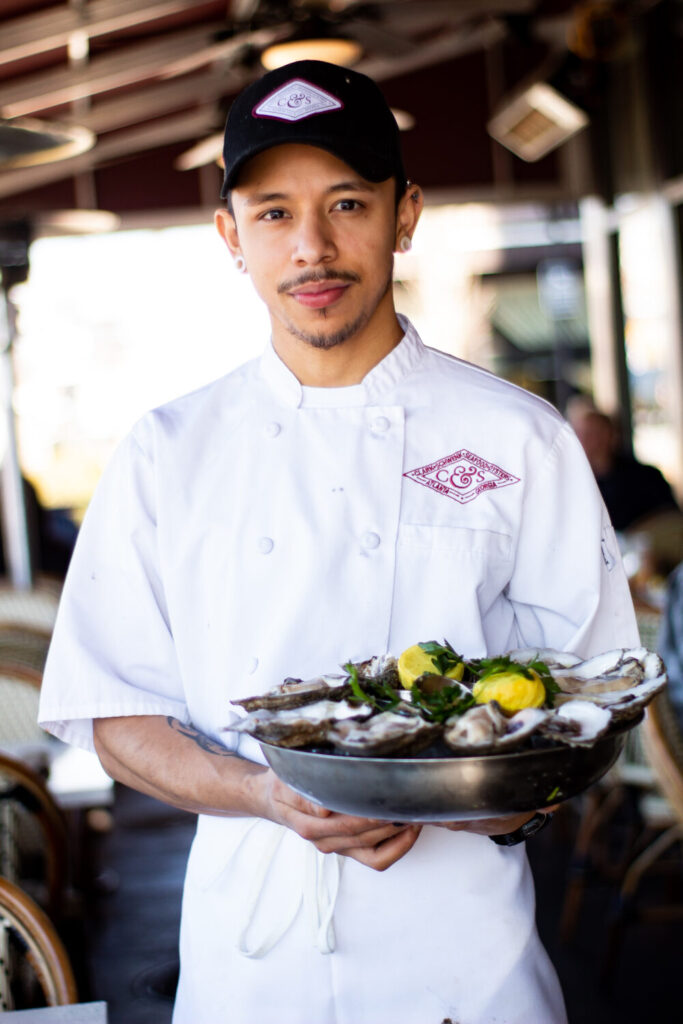man in chef outfit carrying a tray of oysters and lemons on top