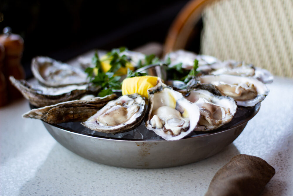 plate of oysters on ice with yellow lemons and green parsley sitting on table.