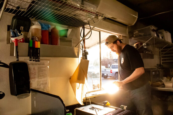 man standing near food truck window with grill and food ingredients around