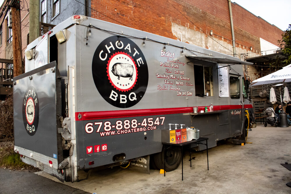 grey food truck with black and red letters with condiment table in front