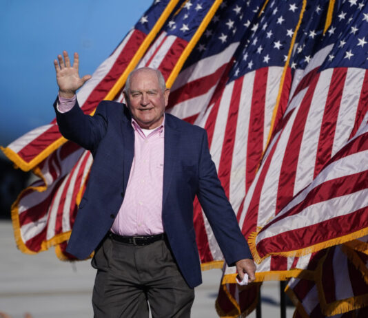 Regents affirm Sonny Perdue to lead Georgia universities white man walking and waving with American flags blowing in the background