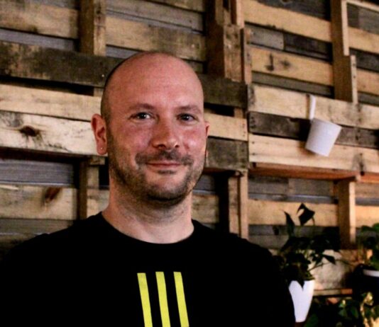 Georgia lawmakers push for suicide prevention efforts in schools suicide prevention school counseling: Jacob Dreiling headshot - middle-aged balding man with brown beard in black t-shirt stands in front of wall covered with recycled wood pallets