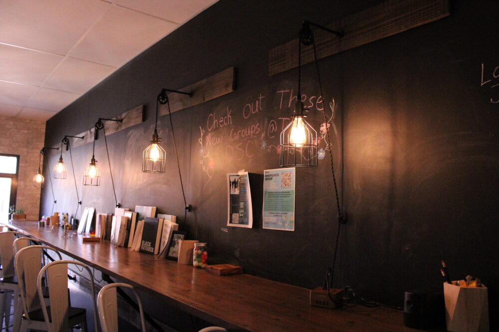 suicide prevention school counseling: Long view of wall with large painted with black chalk board paint and wall lights, with a long attached table witha lot f reading material and lined with chairs.