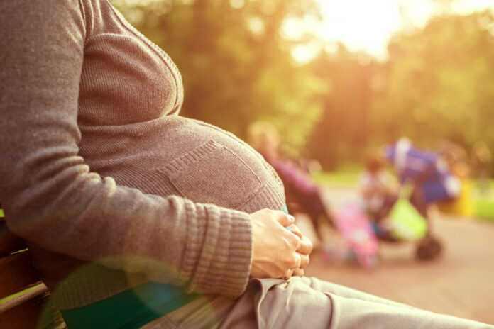 A white pregnant woman sitting on a park bench.