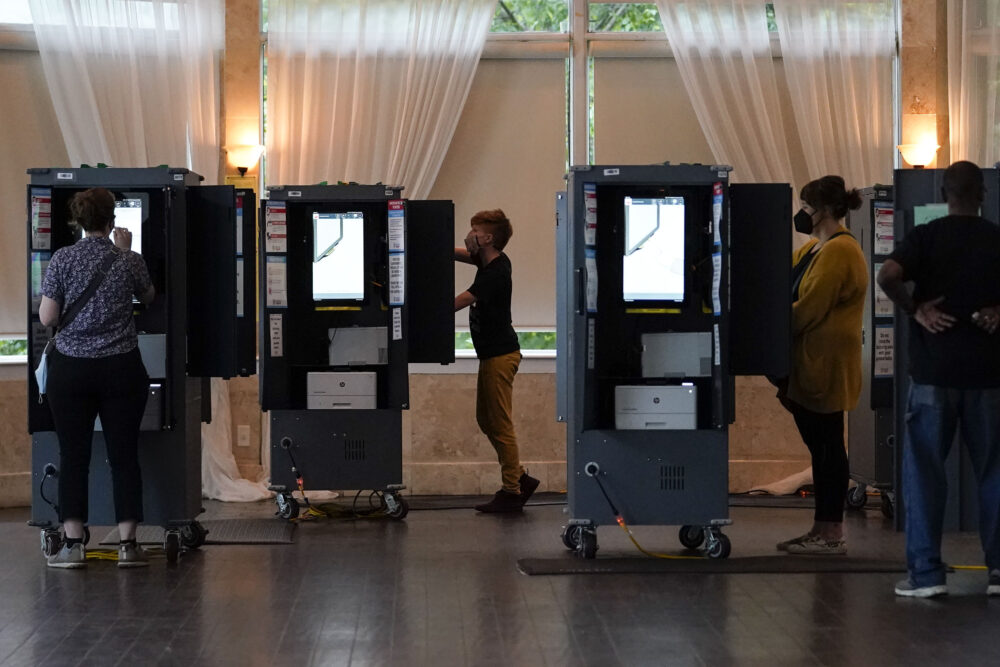 People vote in masks at electric voting machines inside a polling place