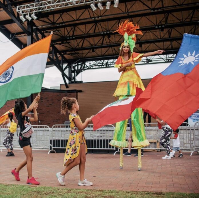 two little girls walking in front of stilt performer waving colorful international flags outside
