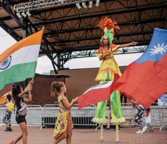 International festival returns to Lawrenceville larger than last year two little girls walking in front of stilt performer waving colorful international flags outside