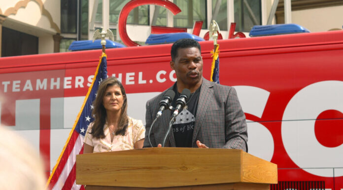 Herschel Walker gets boost from Nikki Haley with Asian American voters Black man in suit jacket stands in front of campaign bus at a podium with woman behind him