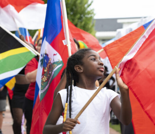 Lawrenceville festival celebrates immigrant stories, food and culture A young Black girl carries a red flag with other people in a parade