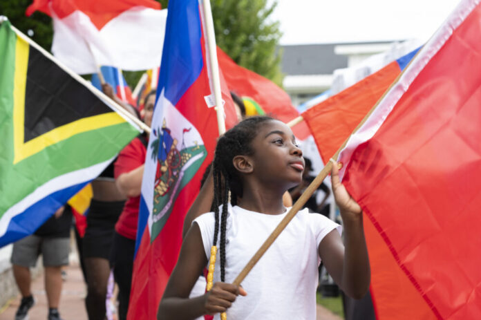 A young Black girl carries a red flag with other people in a parade