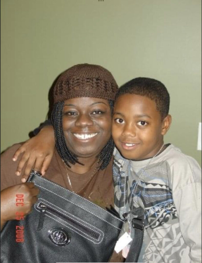 Black woman wearing brown hat poses with young boy and a black purse