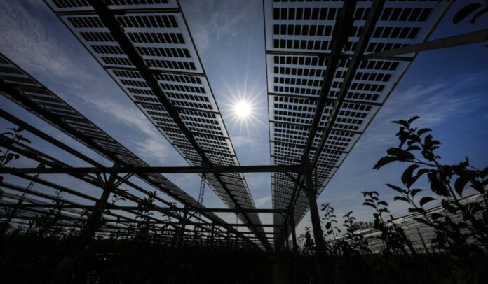 Line of black solar panels shot from below with sun and blue sky above