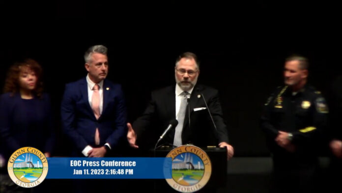 Four people at press conference in uniforms and suits black backdrop