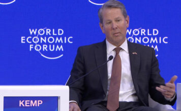 Kemp speaks on panel at World Economic Forum White man sitting in a chair on stage speaking in a suit.