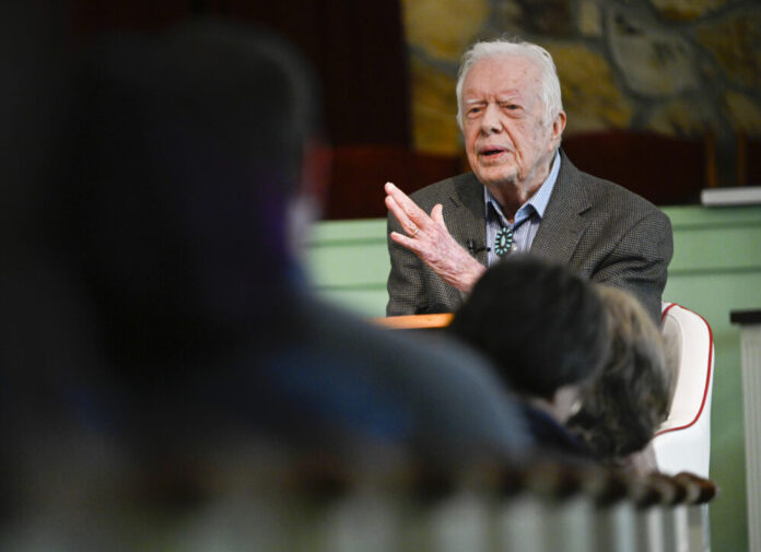 Former President Jimmy Carter in suit inside church talking to microphone