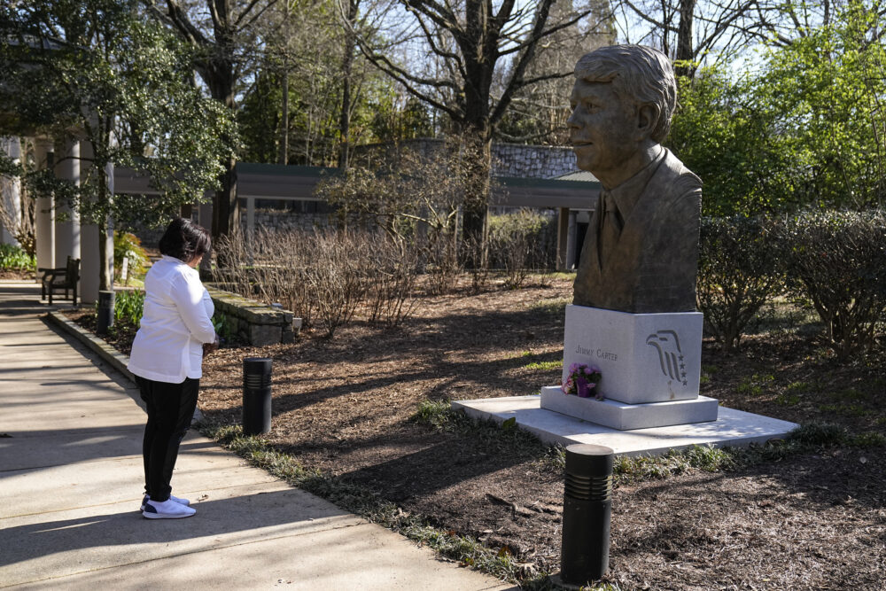 woman in white jacket outside in front of statue of former president jimmy carter