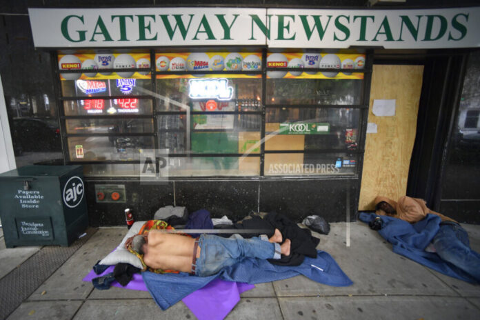 Two men sleeping on the ground outside of a newsstand on the street
