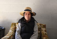 Athens homeless camp offers access to permanent housing for residents in temporary camp site White woman in in straw hat wearing a bandage across her nose sits on a floral chair in front of white background.